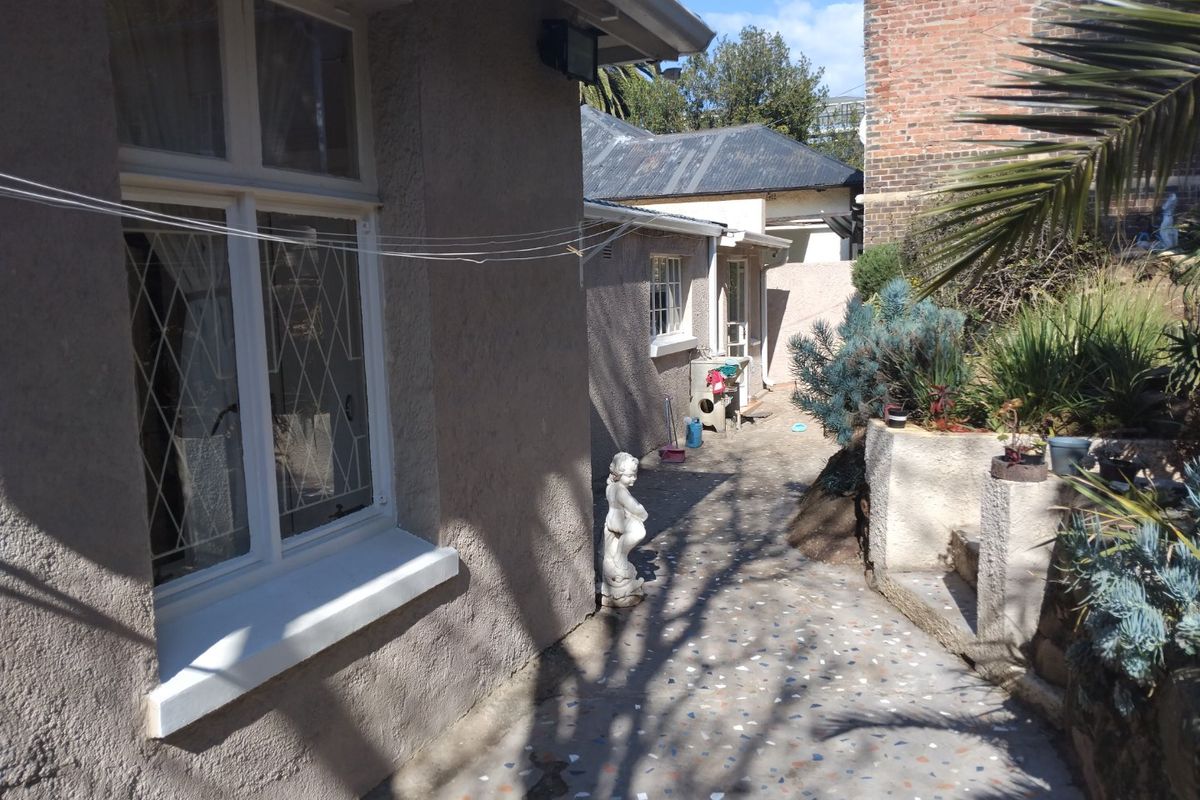 Rear exterior view showing a paved walkway, retaining wall, and building facade with casement windows.