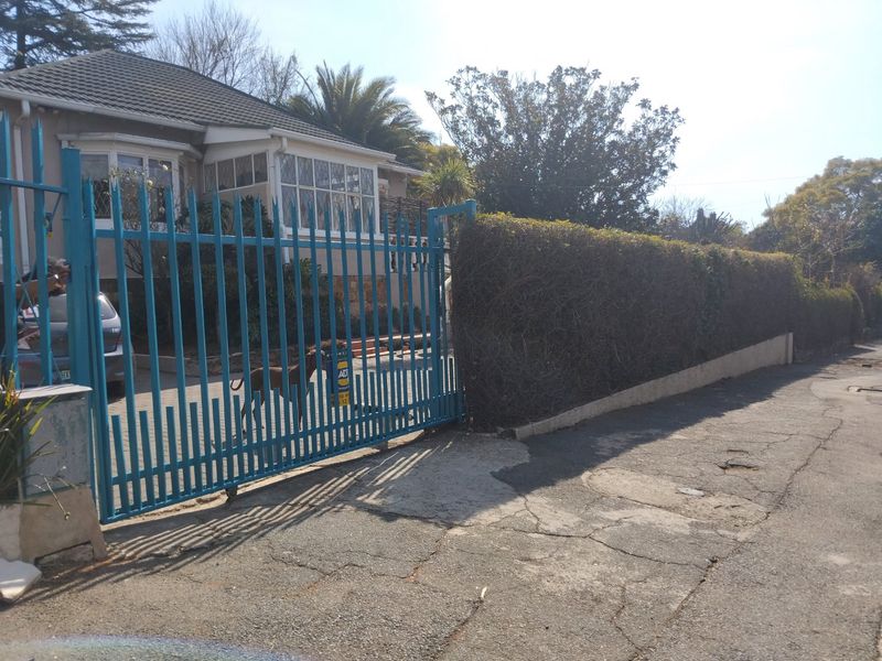 Front view of the property featuring a metal sliding gate, paved driveway, and established perimeter hedge.