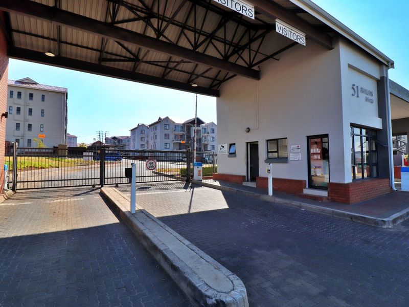 The secure entrance to the apartment complex features a guard house, boom gate, and paved driveway access for visitors and residents.