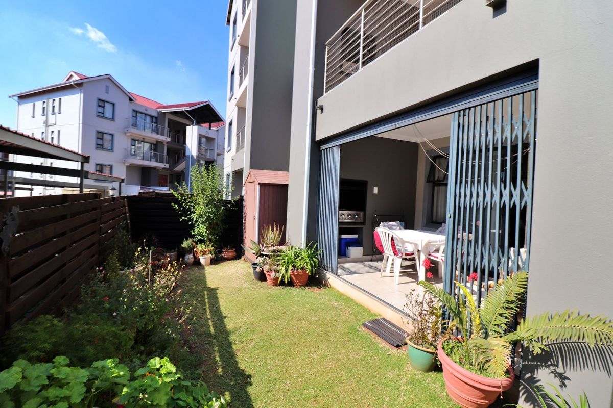 Rear view of the apartment featuring a private garden, lawn, timber fencing, and a covered patio area with a built-in braai and security gate.