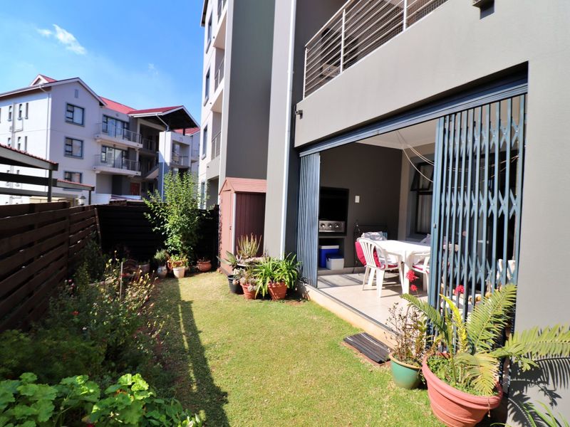 Rear view of the apartment featuring a private garden, lawn, timber fencing, and a covered patio area with a built-in braai and security gate.