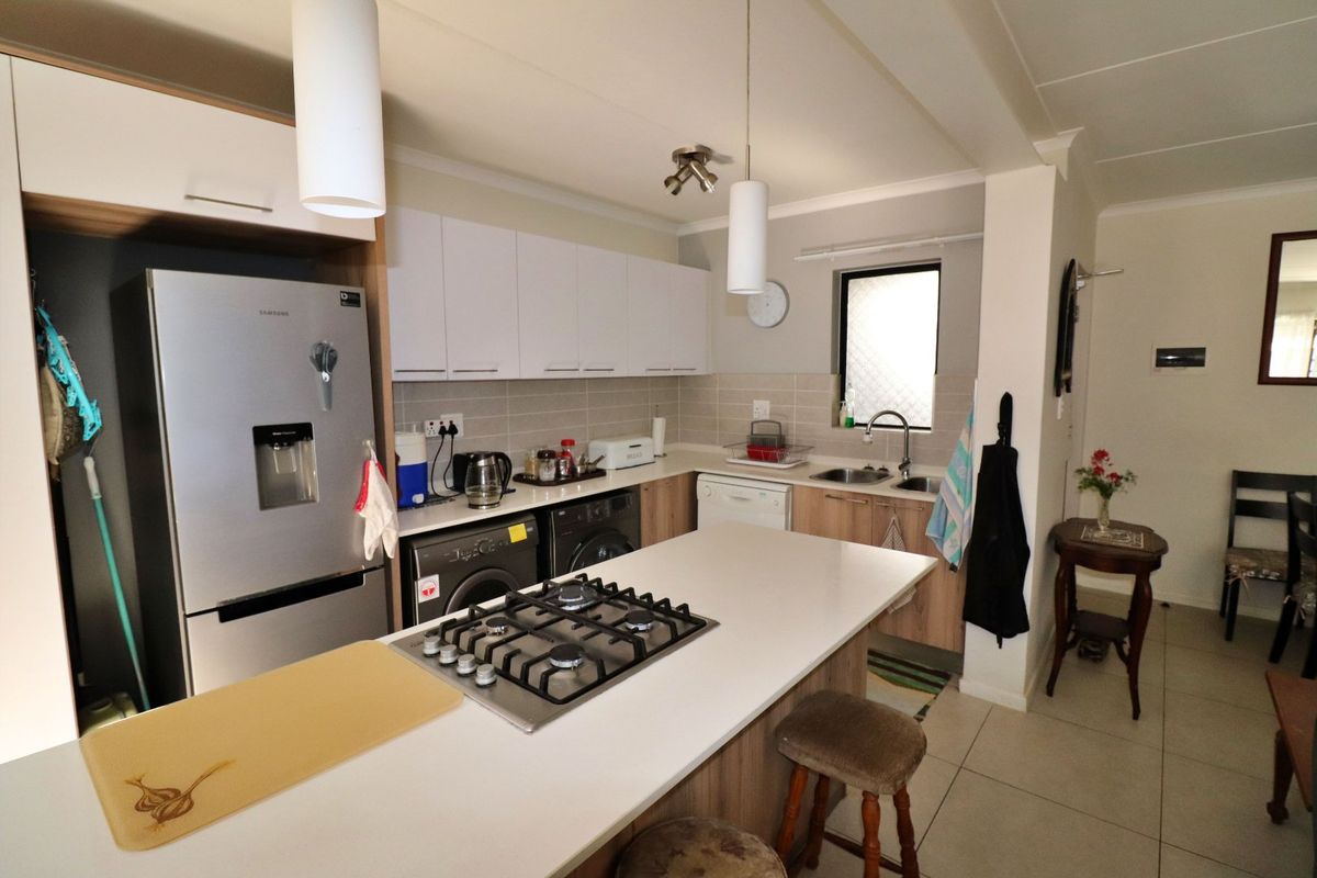 Modern kitchen featuring a central island with a gas hob, ample built-in cabinetry, tiled backsplash, and double sink, offering a functional and well-lit workspace.