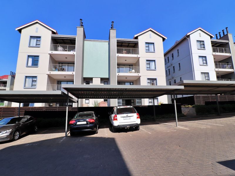 Front elevation of a multi-story apartment complex featuring covered parking bays, paved driveway, and private balconies for each unit.