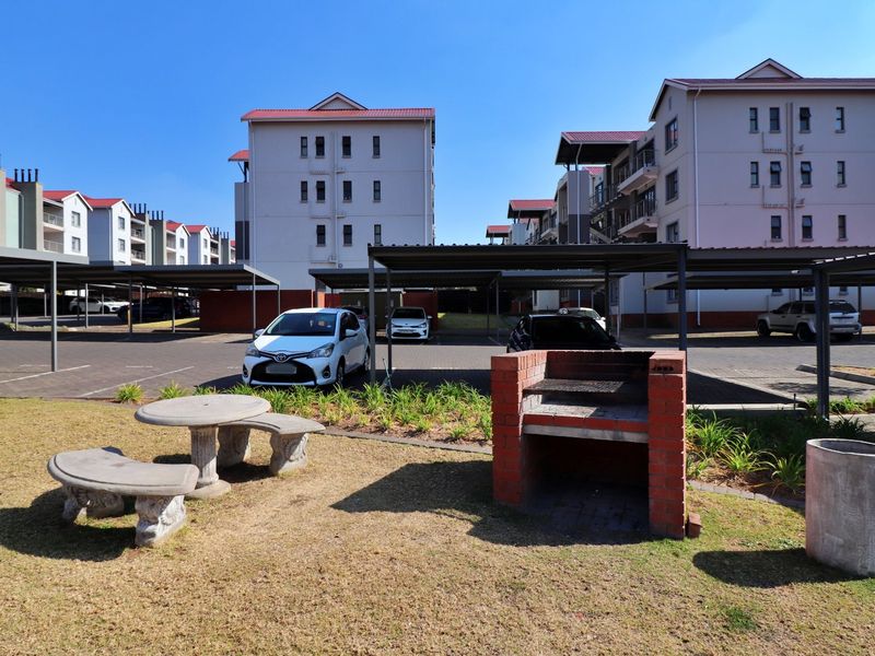 Communal outdoor area featuring a brick braai, landscaped garden, and covered parking bays within the apartment complex.