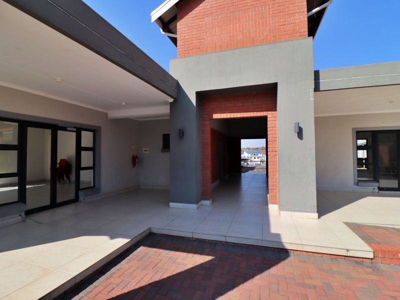 A well-maintained exterior rear courtyard featuring tiled patio areas, brick paving, and modern aluminium-framed glass doors leading into the apartment.