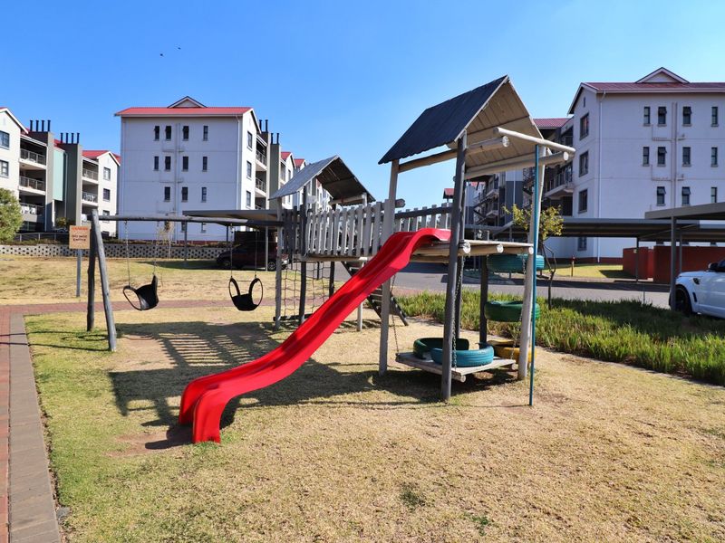 Communal outdoor area featuring a children's playground set, paved pathways, and landscaped lawn situated within an apartment complex.