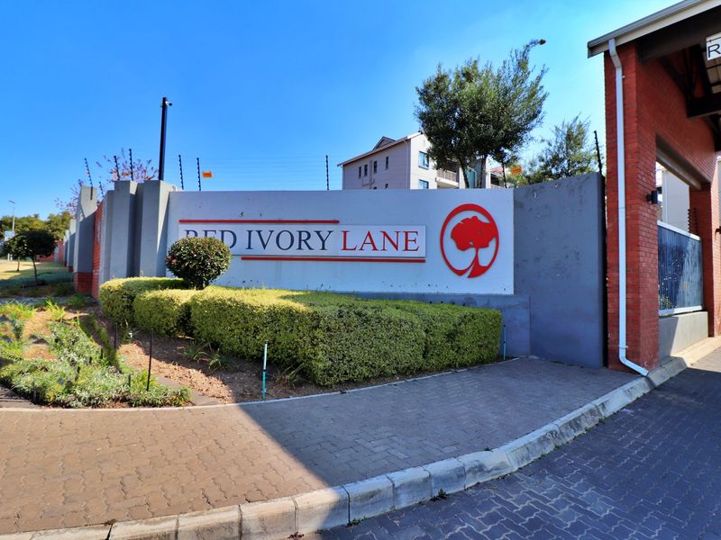 The entrance to Red Ivory Lane complex, featuring a prominent signage wall, paved driveway, and secure gated access with electric fencing.