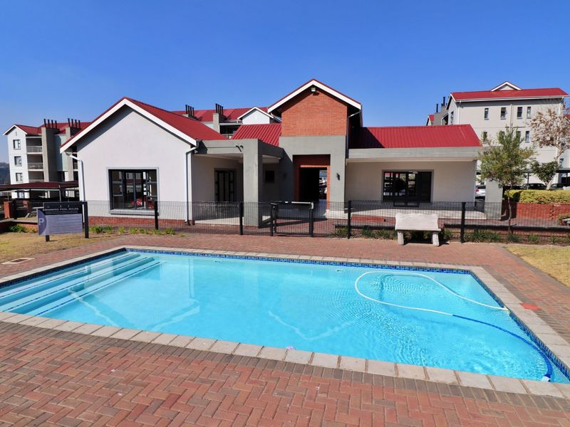 A well-maintained communal swimming pool area featuring brick paving, metal fencing, and a view of the apartment complex building.