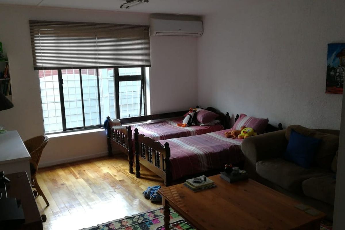 A bedroom featuring timber flooring, a wall-mounted split-system air conditioner, and a window fitted with security bars and venetian blinds.