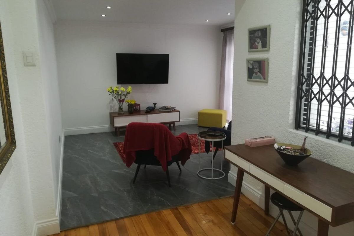 A living room featuring a mix of hardwood and dark tiled flooring, recessed lighting, and a security gate on the window.