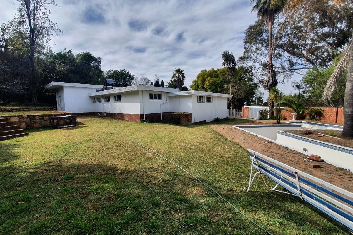 Rear view of the property featuring a swimming pool, lawn area, stone retaining wall, and solar water heating system on the roof.