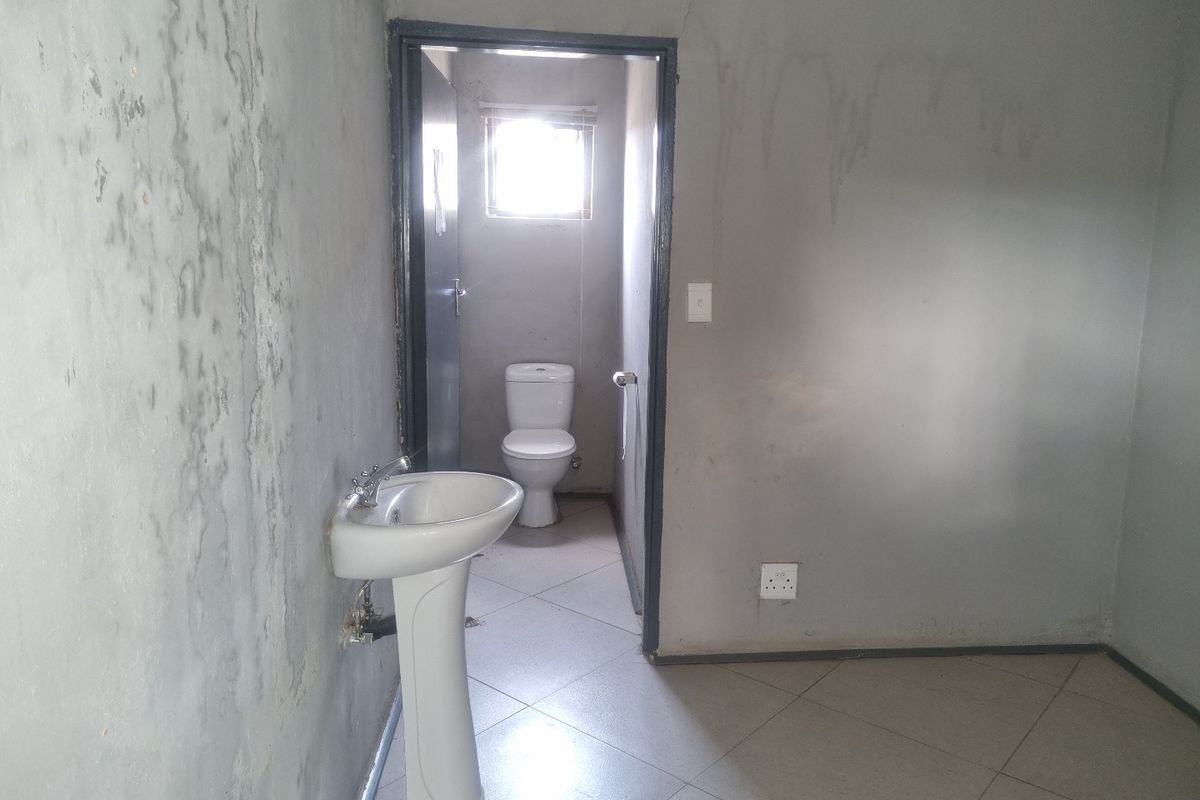 A basic commercial restroom area featuring a pedestal basin and a separate toilet cubicle with tiled flooring and unfinished wall surfaces.