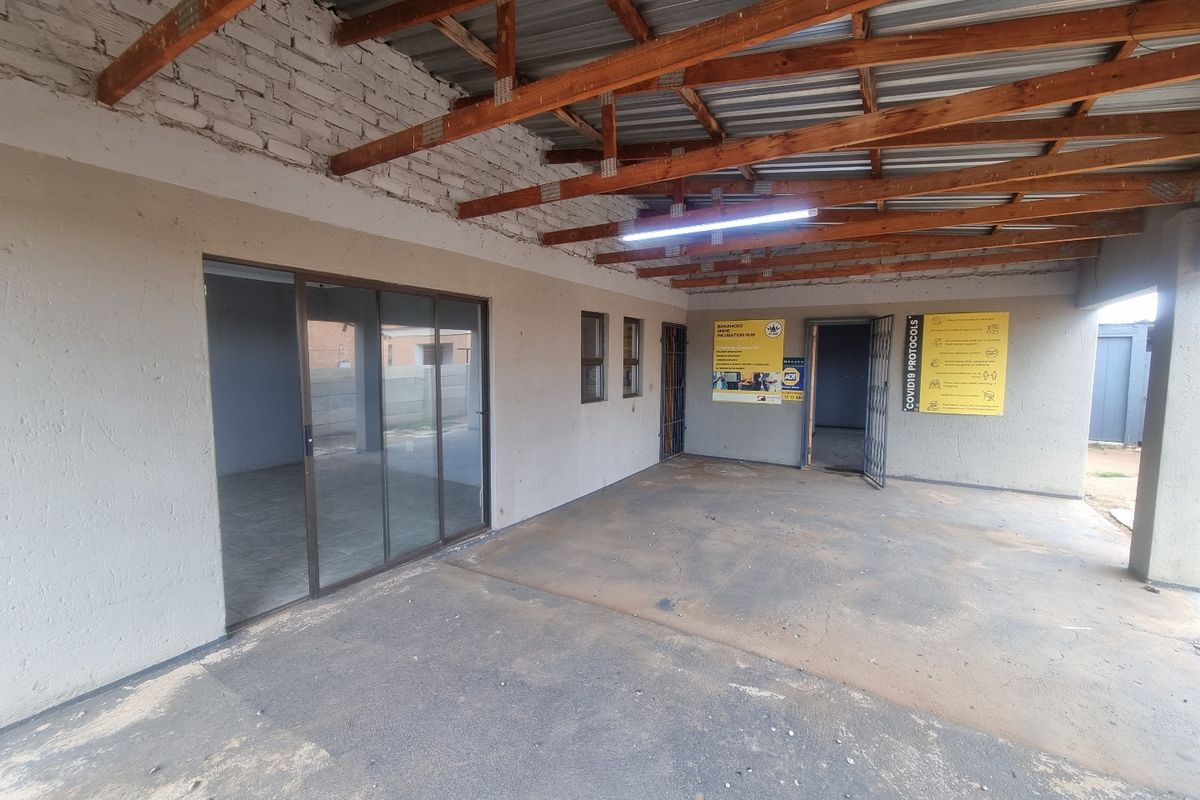 A covered outdoor patio or utility area featuring exposed timber roof beams, concrete flooring, and sliding glass door access to the interior.