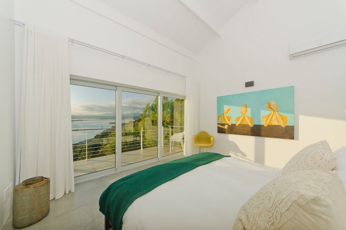 Bright bedroom featuring a vaulted ceiling, split-system air conditioning, and large sliding glass doors opening to a balcony with scenic water views.