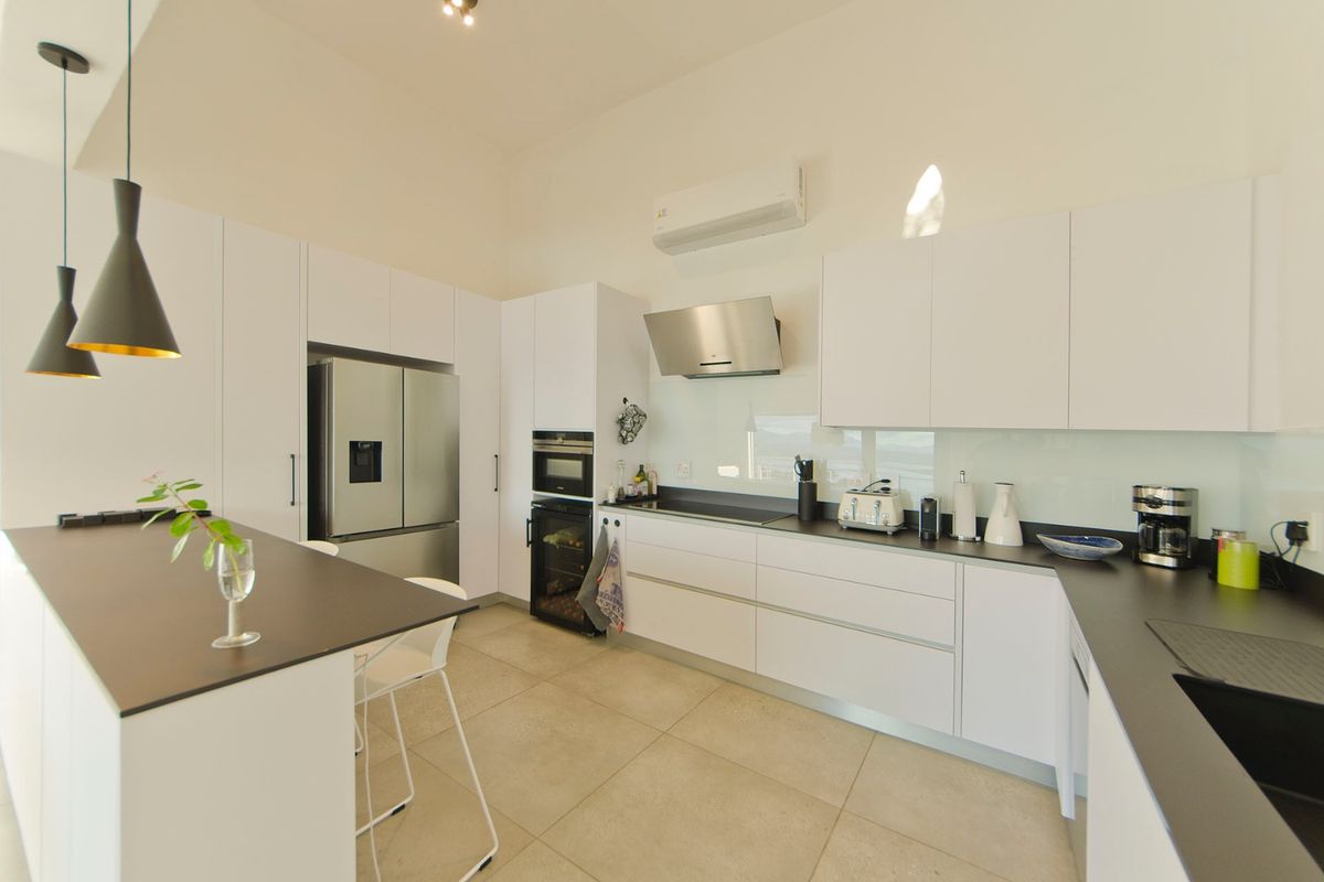 Modern kitchen featuring sleek white cabinetry, dark countertops, a central island, built-in oven, extractor fan, and tiled flooring.