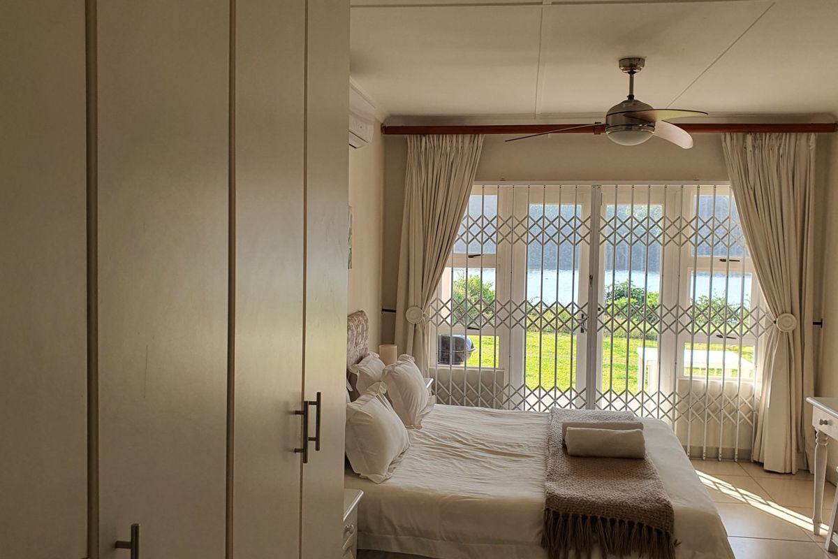 A well-lit bedroom featuring built-in cupboards, a ceiling fan, and sliding glass doors with security gates leading to an outdoor area.
