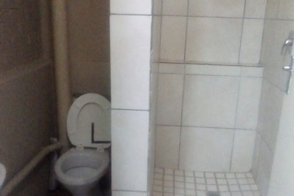 A basic bathroom featuring a toilet and a tiled shower enclosure with visible plumbing and dated finishes.