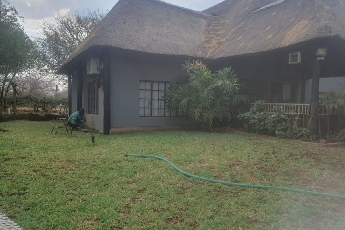 Rear view of a house featuring a traditional thatched roof, timber decking, and a surrounding garden area.