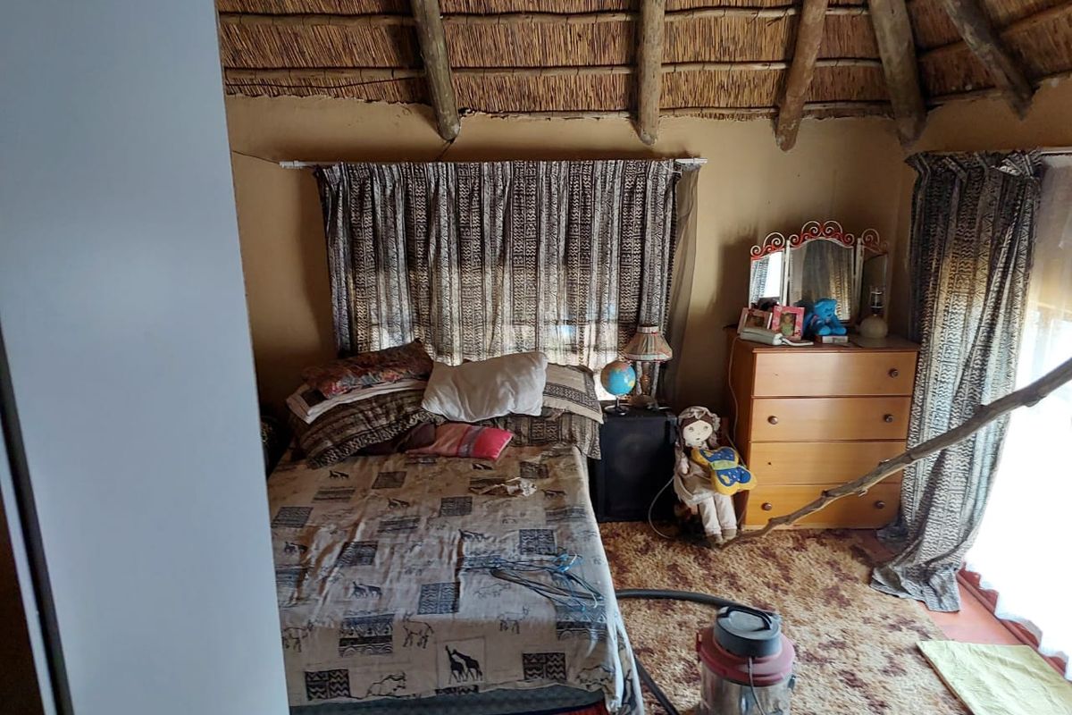 A bedroom featuring a traditional thatched roof with exposed timber rafters, offering a rustic aesthetic in need of cosmetic updates.