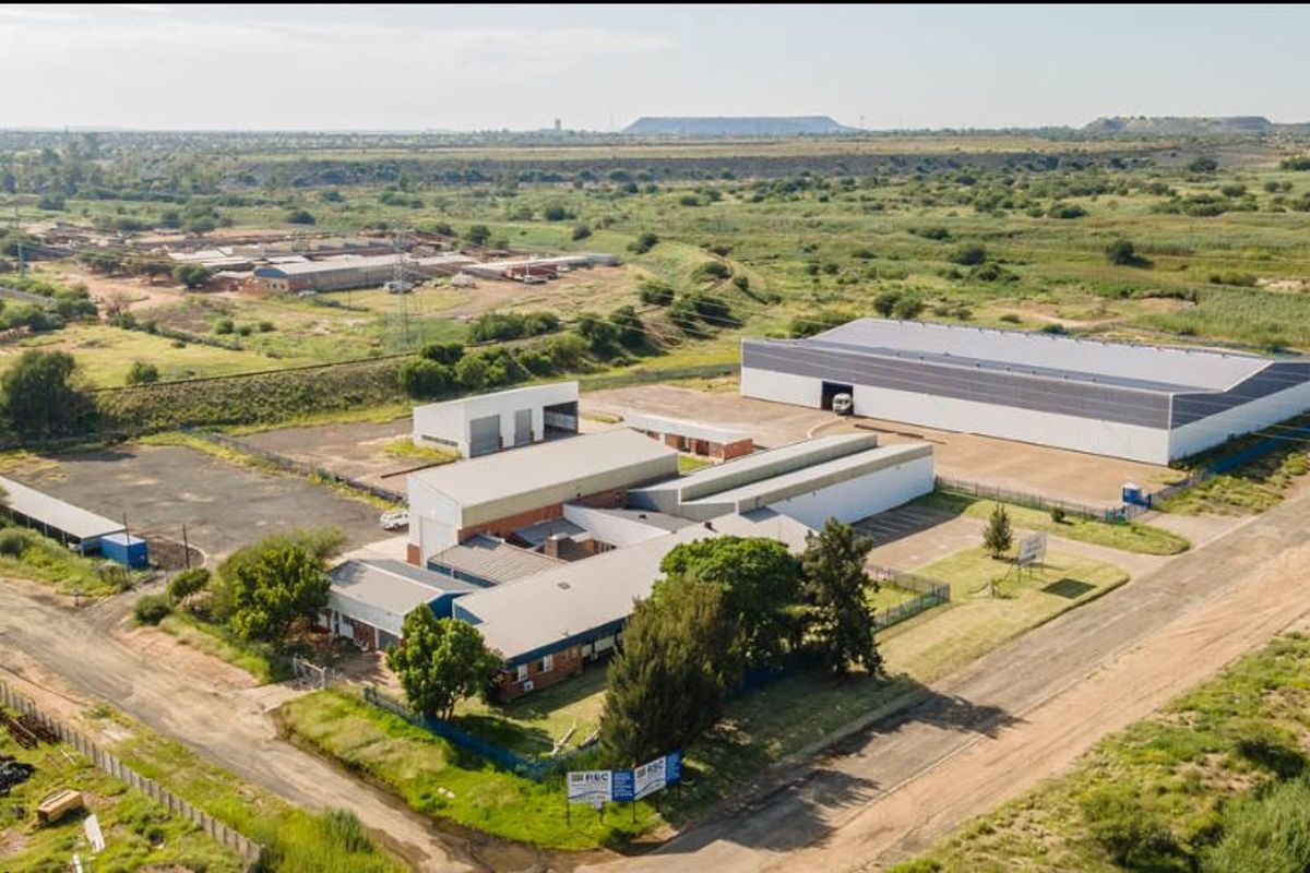 Aerial view of an industrial property complex featuring multiple warehouse buildings, paved access areas, and perimeter fencing in a spacious site.