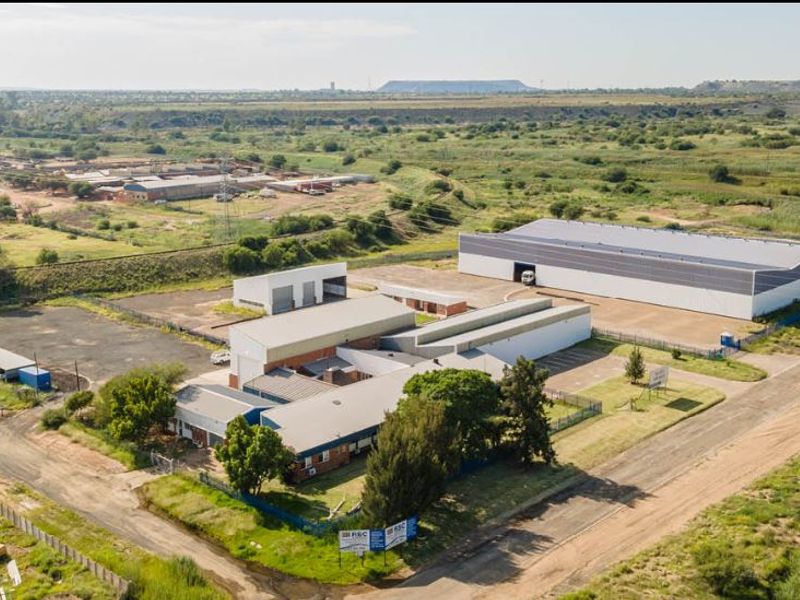 Aerial view of an industrial property complex featuring multiple warehouse buildings, paved access areas, and perimeter fencing in a spacious site.