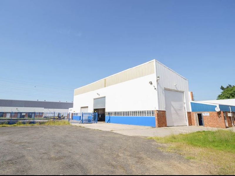 Industrial warehouse facility featuring large roller shutter doors, metal cladding, and a spacious asphalt yard area with perimeter security fencing.