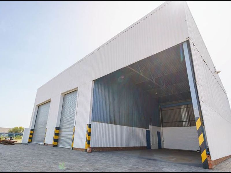 Industrial warehouse facility featuring high-clearance roller shutter doors, durable corrugated metal cladding, and a spacious paved exterior access area.