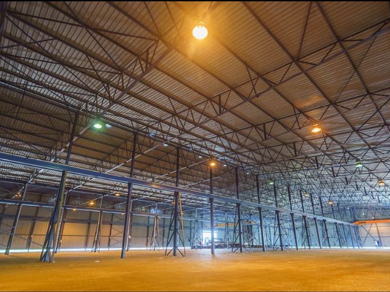 Expansive industrial warehouse space featuring high-clearance steel truss roofing, robust support columns, and durable concrete flooring, suitable for various commercial or storage operations.