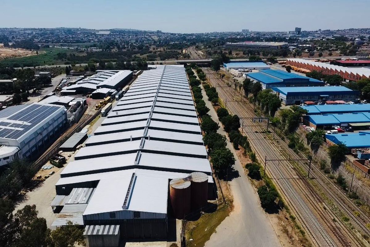 Aerial view of a large industrial warehouse facility featuring metal roofing, adjacent silos, and direct access to a railway siding.