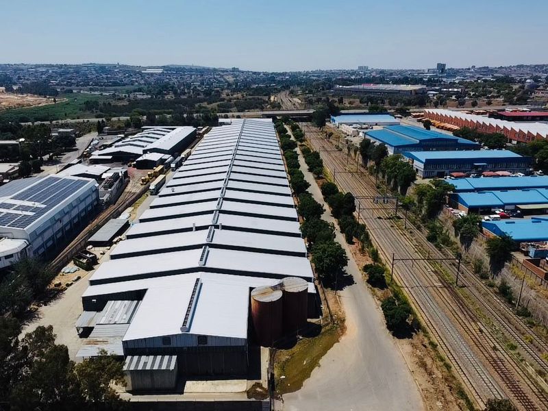 Aerial view of a large industrial warehouse facility featuring metal roofing, adjacent silos, and direct access to a railway siding.