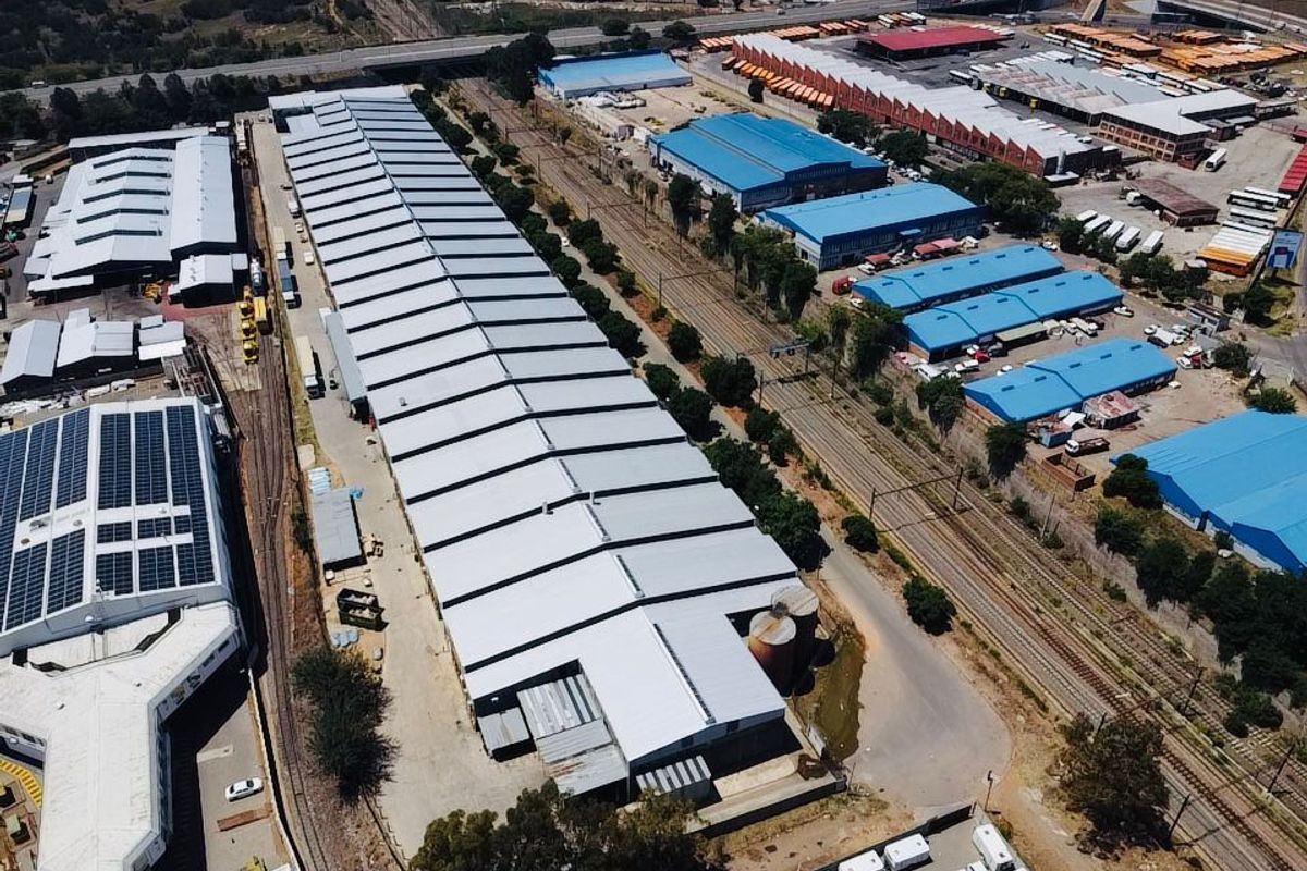 Aerial view of an extensive industrial warehouse facility featuring large metal-roofed structures, dedicated railway access, and storage silos within a commercial precinct.