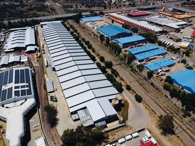 Aerial view of an extensive industrial warehouse facility featuring large metal-roofed structures, dedicated railway access, and storage silos within a commercial precinct.