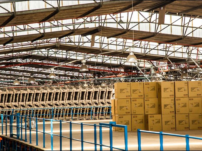 Large industrial warehouse space featuring high-clearance steel roof trusses, translucent roofing for natural light, industrial pendant lighting, and a mezzanine level with safety railings.