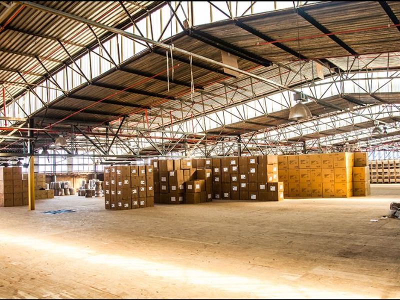 Spacious industrial warehouse featuring high exposed steel roof trusses, corrugated metal roofing, and durable concrete flooring, suitable for storage or manufacturing operations.