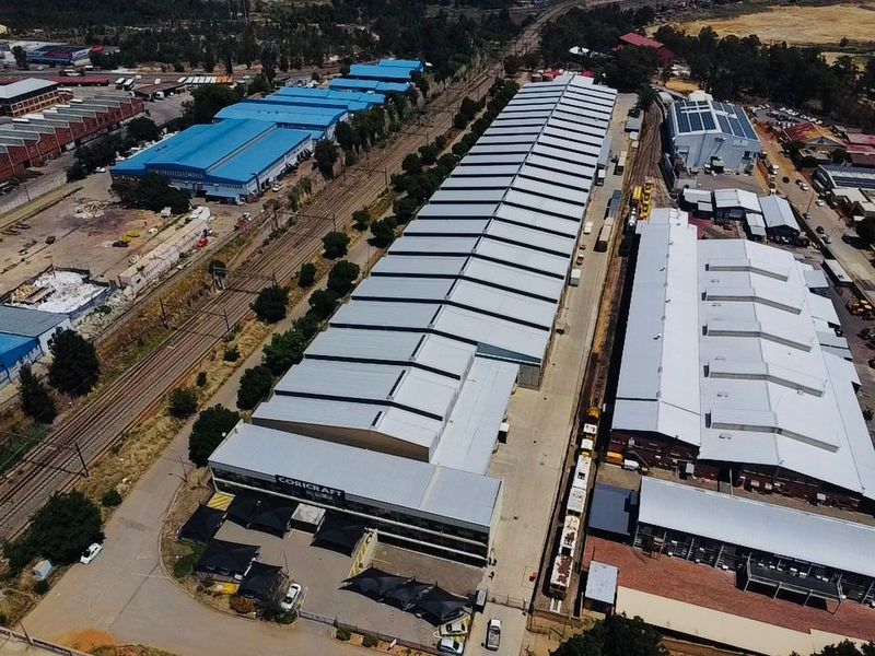 Aerial view of a large industrial warehouse facility featuring extensive metal roofing, dedicated railway siding access, and paved yard space.