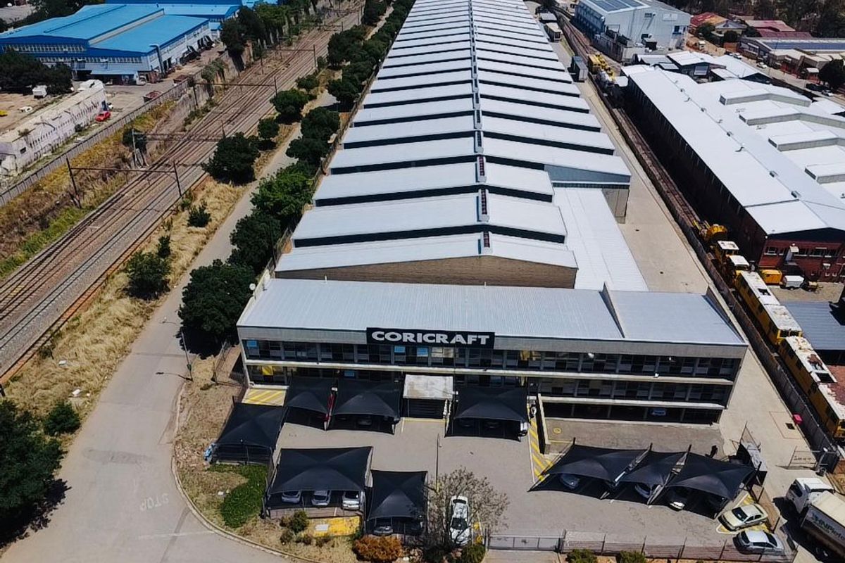 Aerial view of a large industrial warehouse facility featuring a sawtooth roof design, multi-level office frontage, and dedicated paved parking with shade cloth structures.