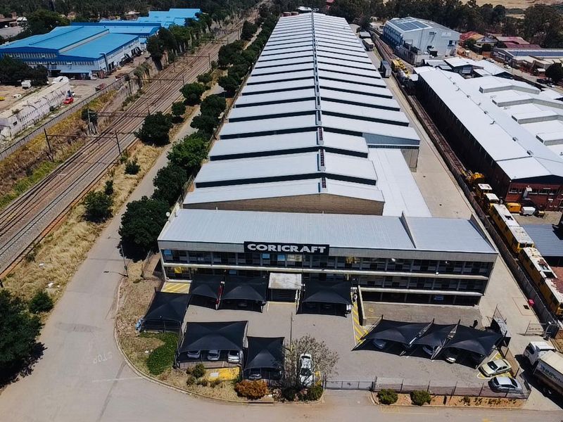 Aerial view of a large industrial warehouse facility featuring a sawtooth roof design, multi-level office frontage, and dedicated paved parking with shade cloth structures.