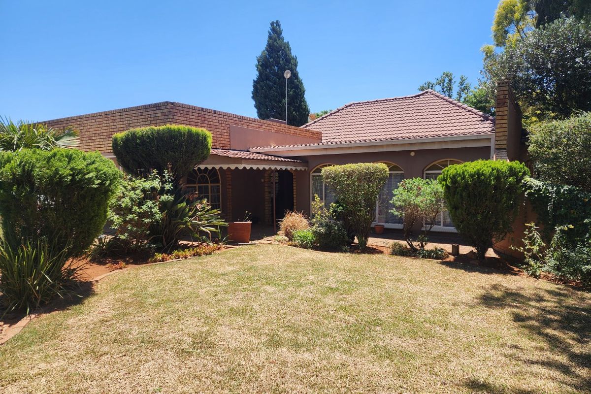 Rear view of a brick house featuring a tiled roof, arched windows, a covered patio area, and a well-established garden.