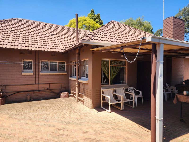 Rear view of the house featuring a paved patio area, covered outdoor space, and traditional brick facade with tiled roofing.