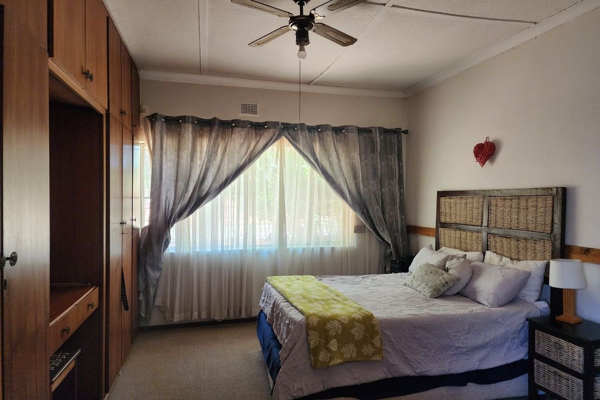 A bedroom featuring built-in wooden cupboards, a ceiling fan, and carpeted flooring, offering a functional space with potential for cosmetic updates.