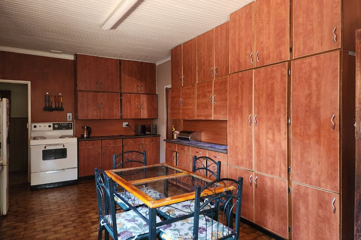 A dated kitchen featuring extensive wood-finish cabinetry, tiled flooring, and a classic freestanding oven, offering significant potential for a modern renovation.