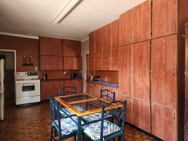 A dated kitchen featuring extensive wood-finish cabinetry, tiled flooring, and a classic freestanding oven, offering significant potential for a modern renovation.