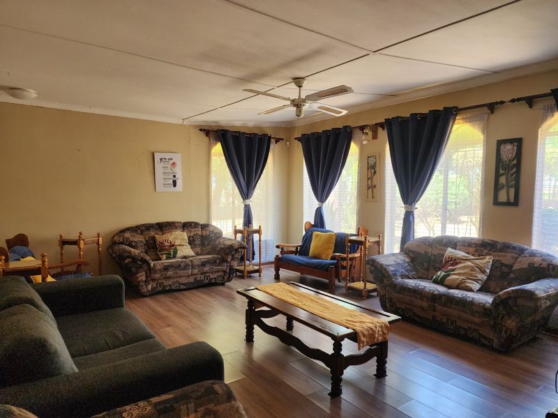 A spacious living room featuring laminate flooring, a central ceiling fan, and large windows with curtain treatments.
