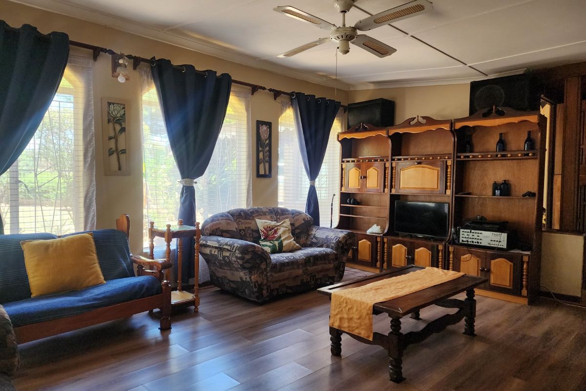 A living room featuring laminate flooring, a ceiling fan, and a large built-in wooden shelving unit.