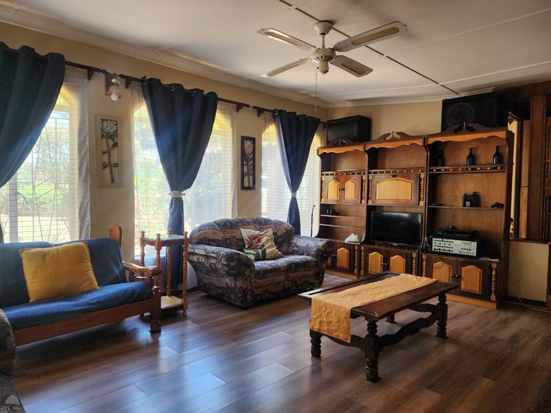 A living room featuring laminate flooring, a ceiling fan, and a large built-in wooden shelving unit.