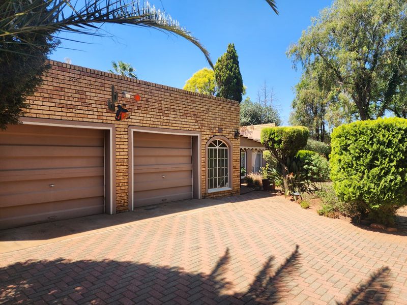 Front view of the property featuring a double garage with brick facade, arched window detail, and a well-maintained paved driveway and garden area.