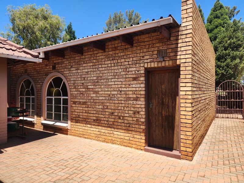 Rear exterior view of a face brick building featuring arched windows, a timber door, and a paved patio area.