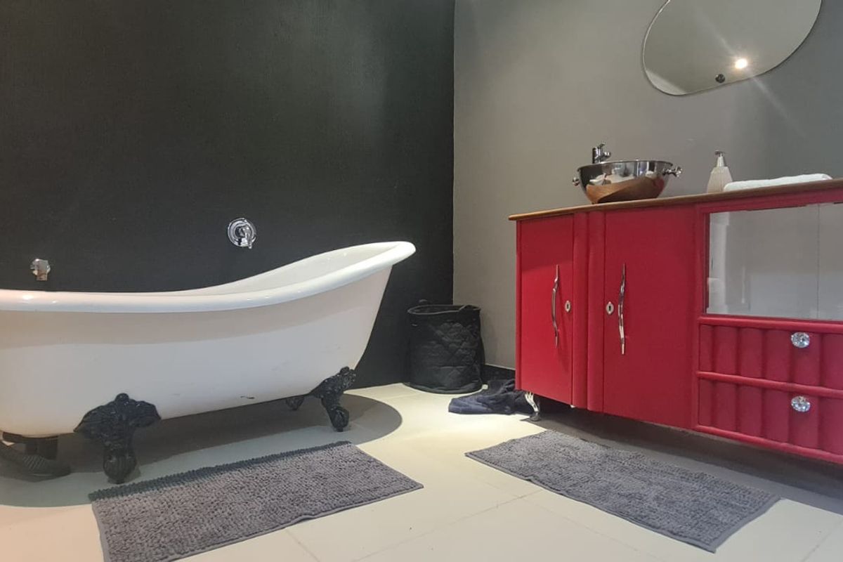 A bathroom featuring a classic clawfoot bathtub, a bold red vanity cabinet with a vessel sink, and dark accent walls.