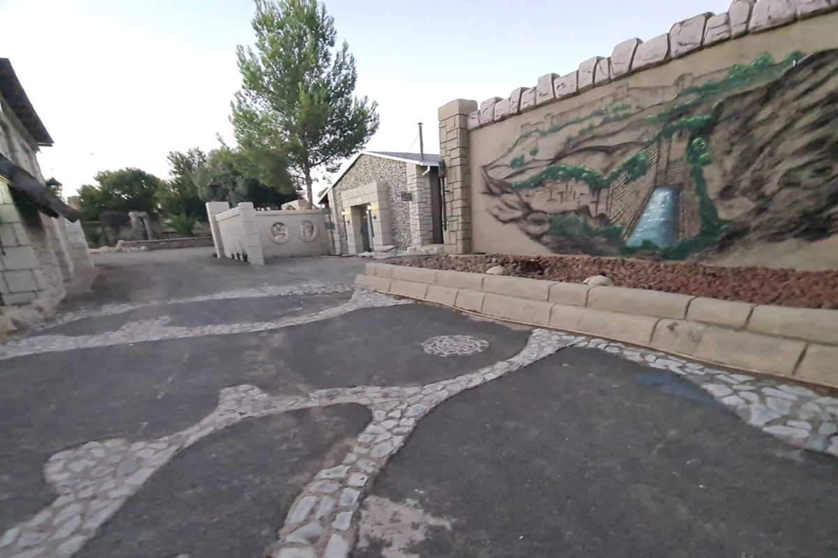 An outdoor courtyard area featuring stone masonry walls, decorative murals, and a paved driveway with stone detailing.
