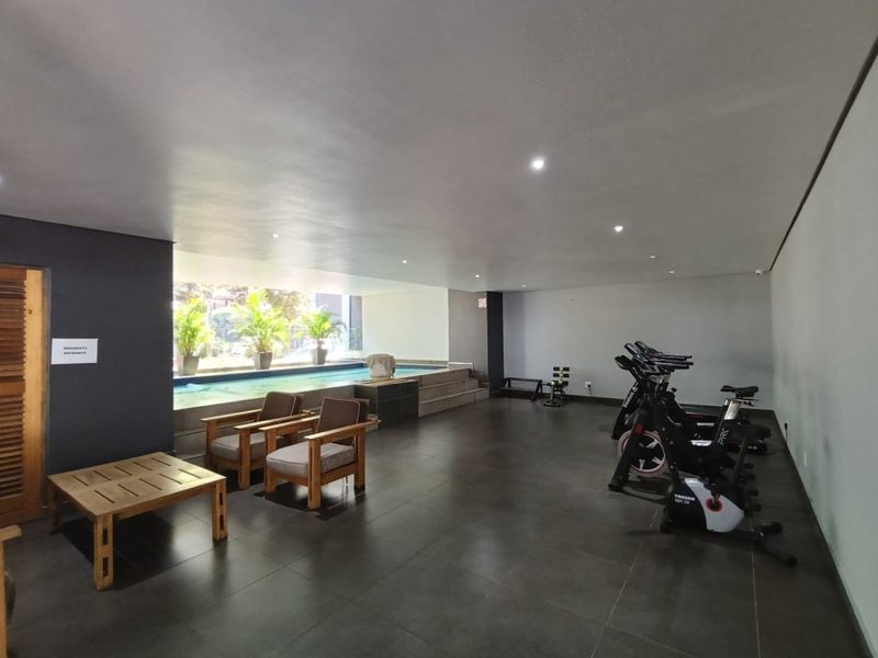 A modern indoor gym facility featuring tiled flooring, recessed lighting, and direct access to an integrated indoor swimming pool area.
